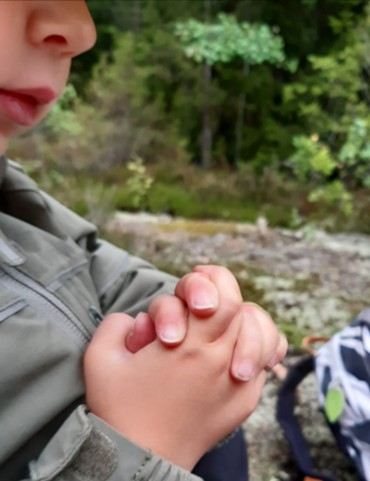 Lapsi istuu kalliolla, metsässä. Kädet ristissä.