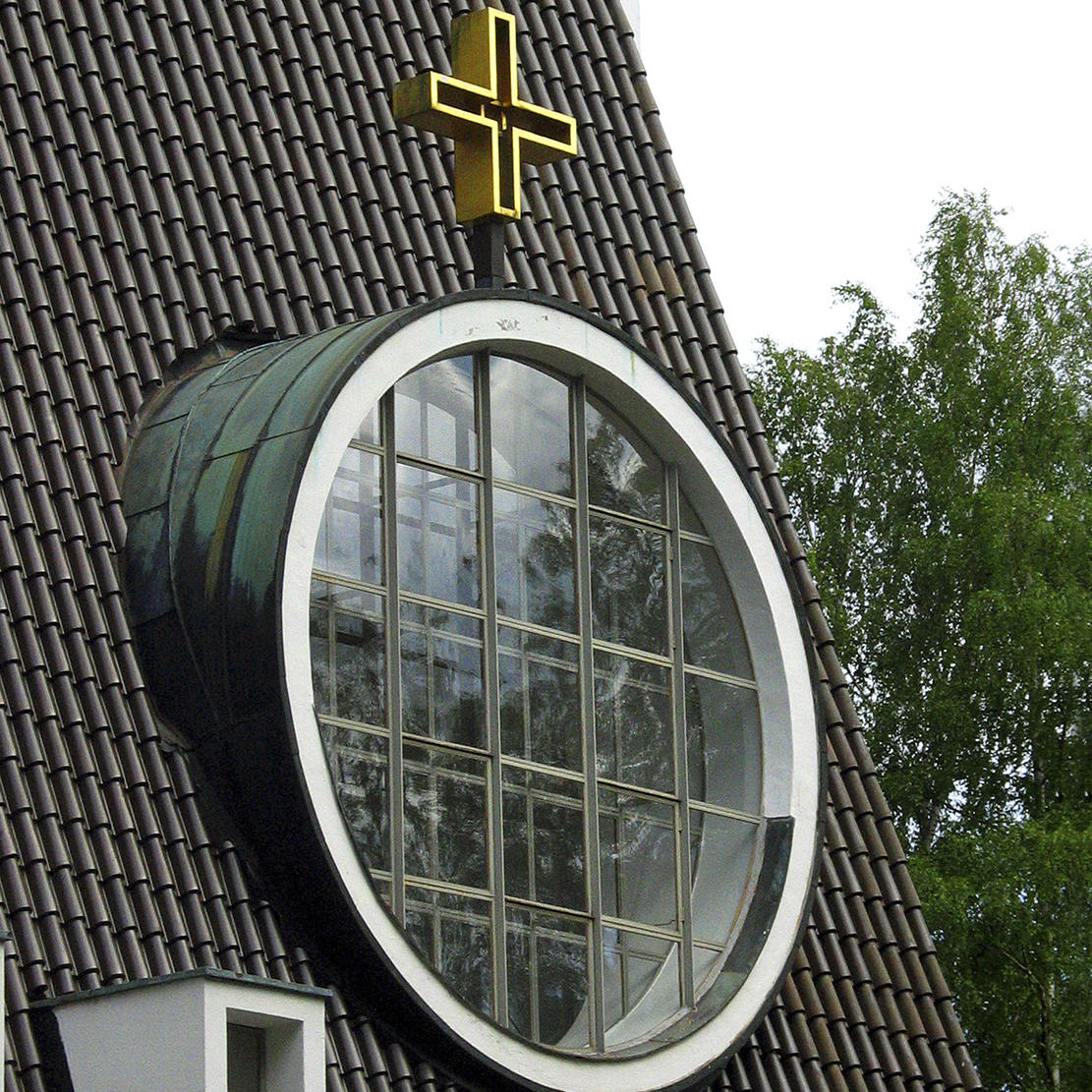Rajamäen kirkon jyrkässä katossa on alttarin oikealla puolella suuri, pyöreä Kristus-ikkuna.