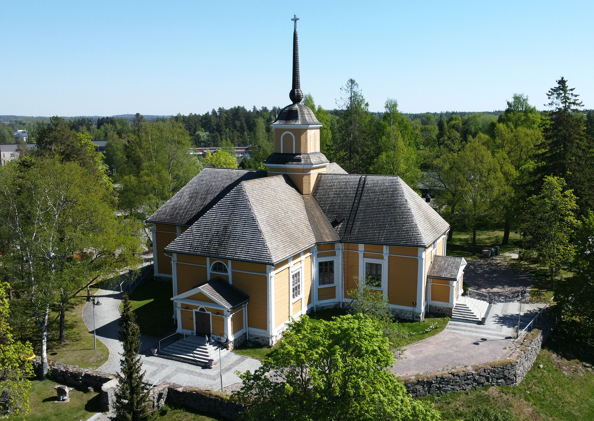 Dronella otettu ilmakuva Nurmijärven kirkosta, joka sijaitsee lehtipuiden ympäröimänä.
