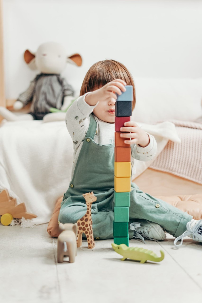 Kuvassa lapsi istuu lattialla ja kokoaa erivärisistä puisista palikoista tornia