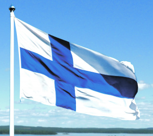 Suomen lippu liehuu taustallaan sininen taivas, jossa kumpupilviä.